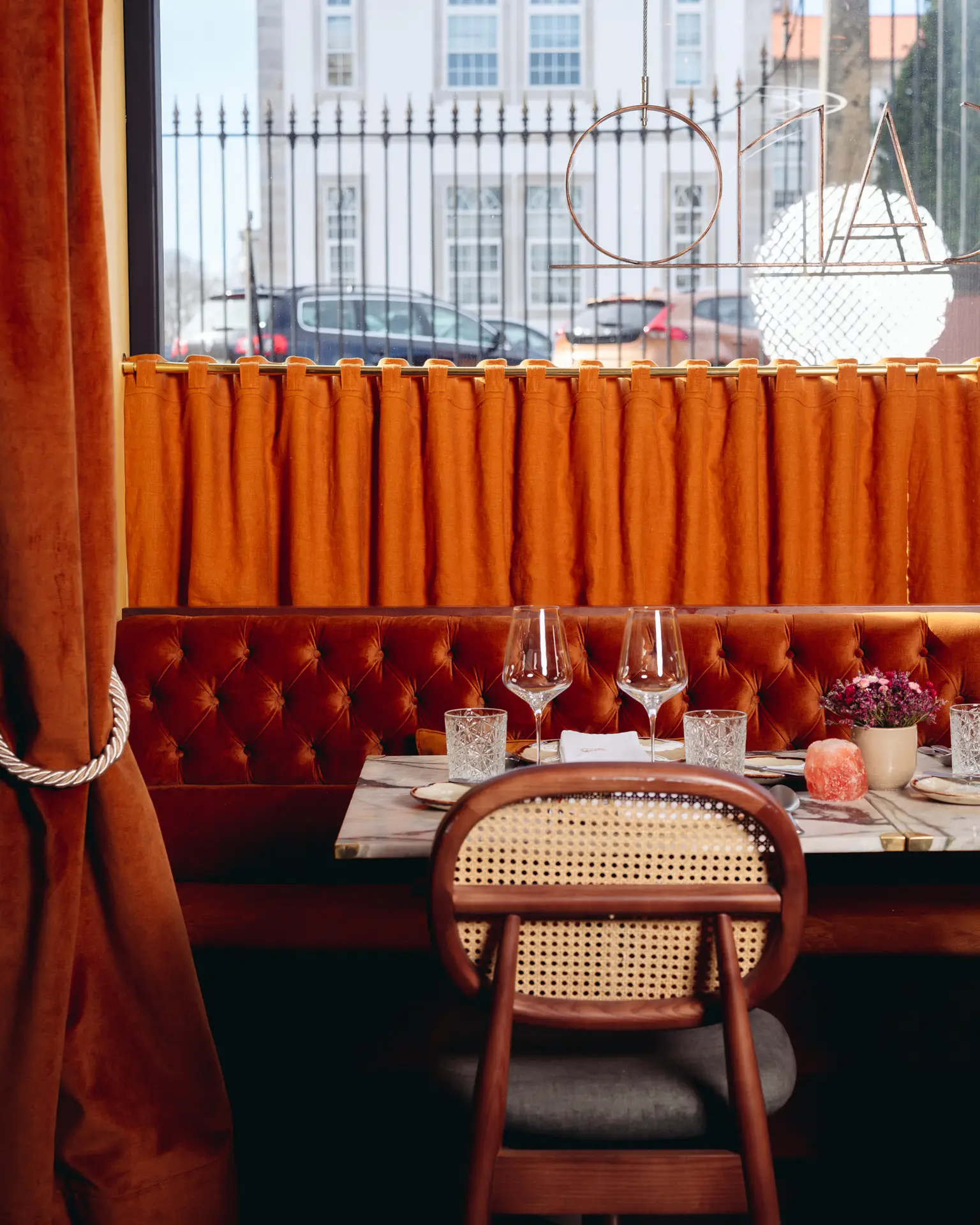 Ambiente acolhedor e sofisticado do Ristorante Toscano com mesa elegantemente posta, vista de uma janela e cortinas laranja.